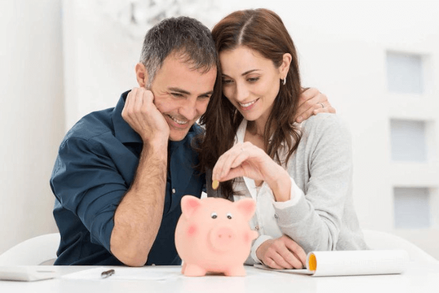 Casal inserindo moeda em cofrinho e sorrindo por conseguirem economizar dinheiro